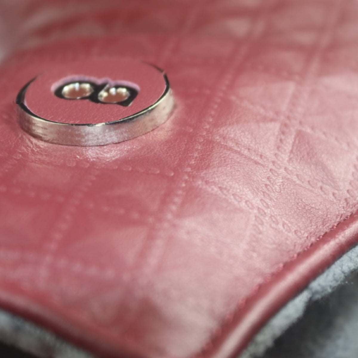 Close-up of a pink quilted leather surface with a silver-tone metal snap button, showing the texture and stitching detail.