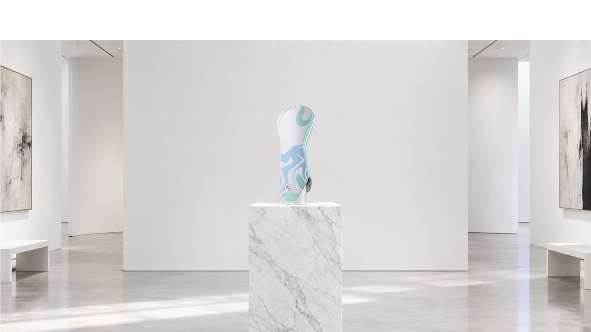 A white leather golf club headcover with a aqua blue and light green abstract design by David Alexander sitting on a plinth in an art gallery.