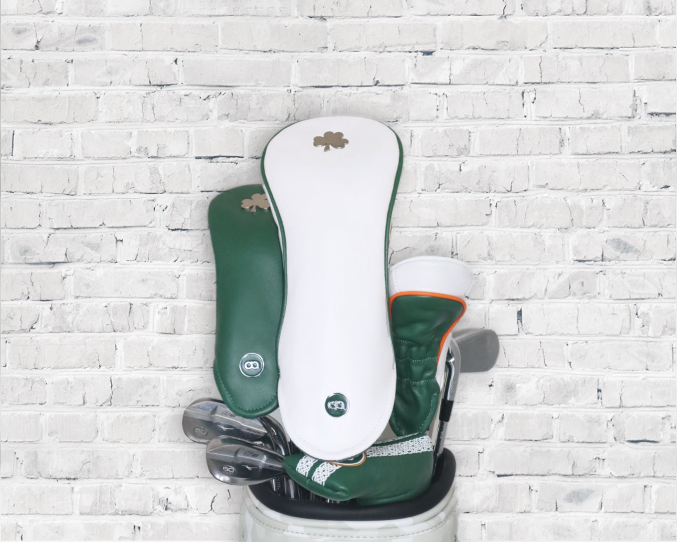 White and green Ireland leather golf club headcover set by David Alexander against a white wall background.