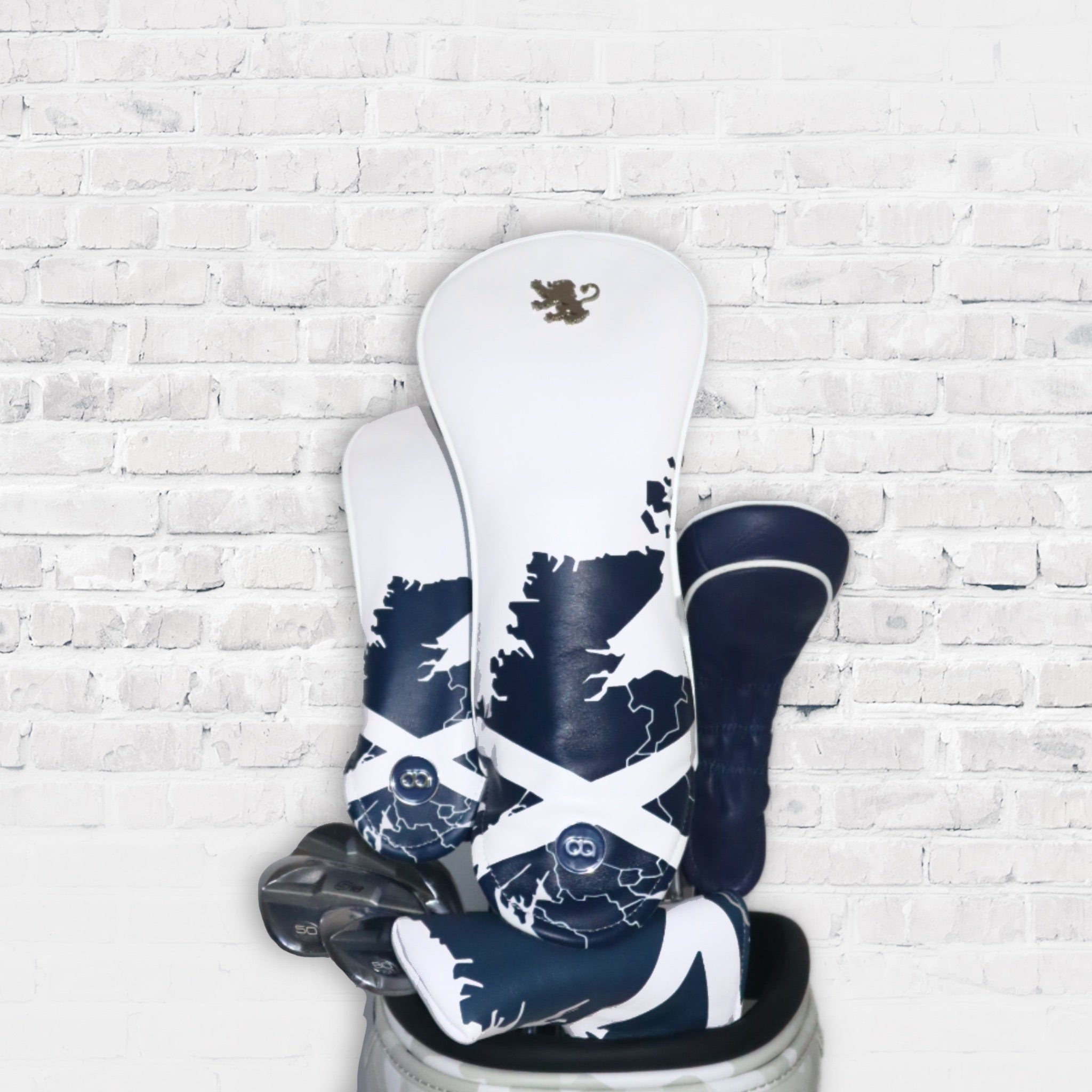 A set of white and blue Scotland leather golf club headcovers against a white wall background.