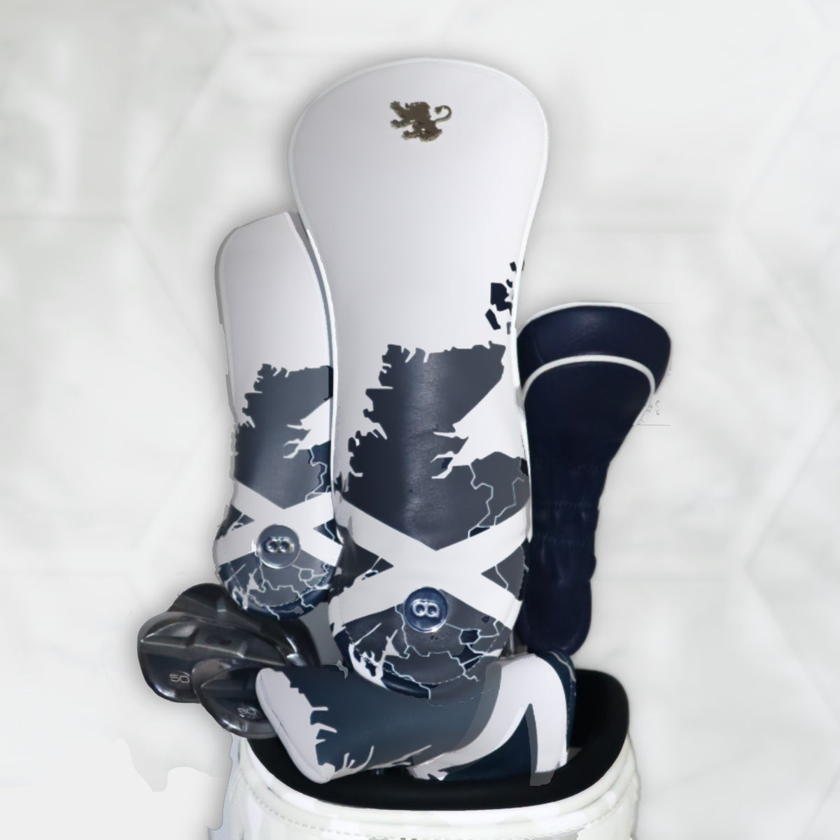A set of white and blue Scotland leather golf club headcovers against a white wall background.