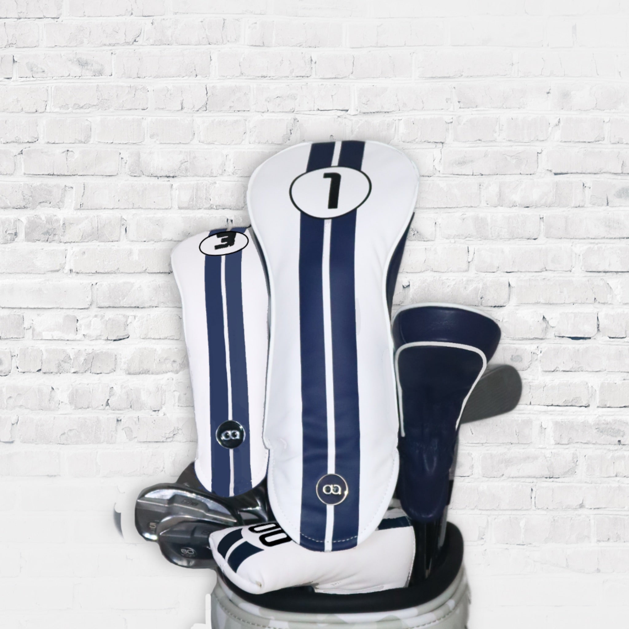 A set of white and blue Racking Line leather golf club headcovers against a white wall background.