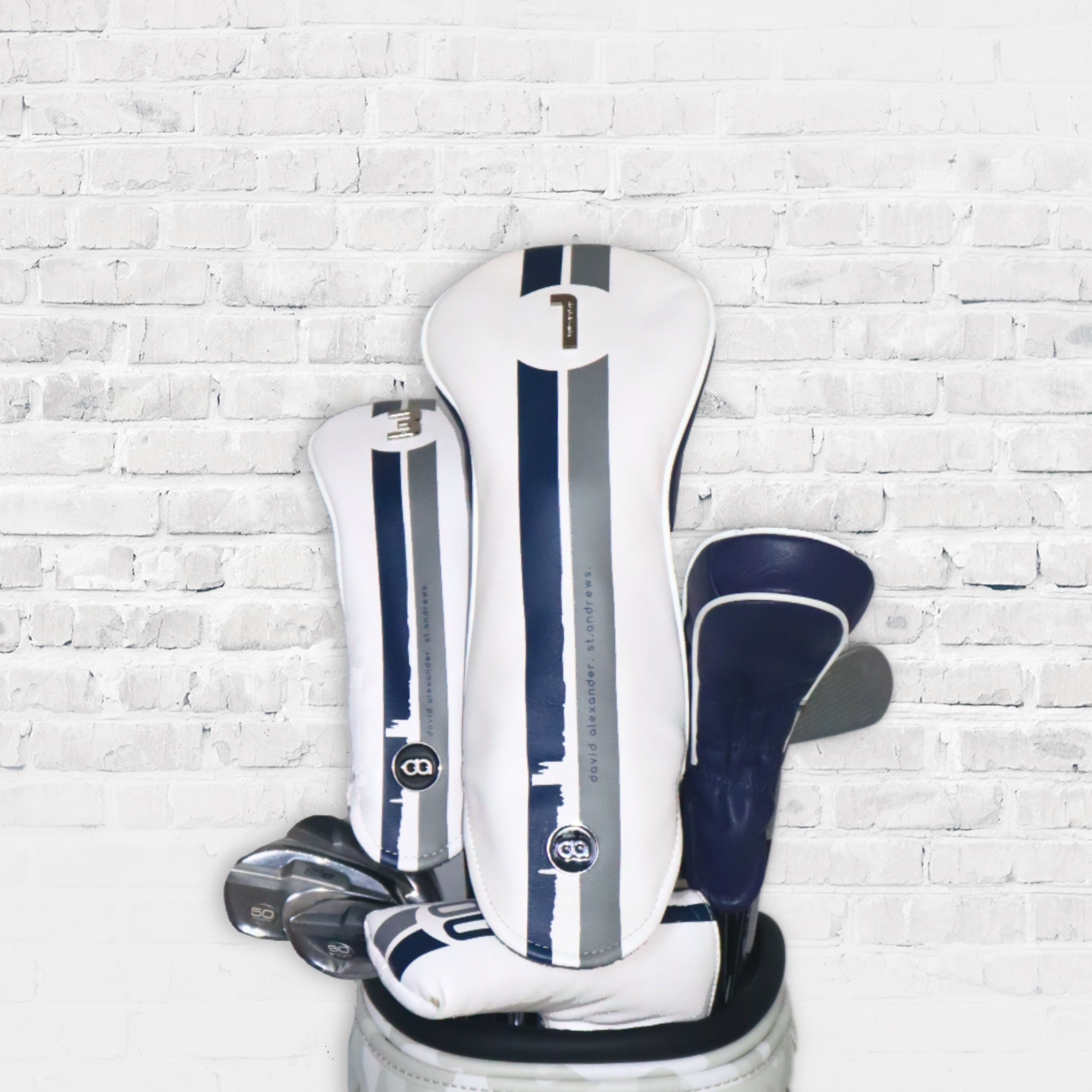 A set of white and blue St. Andrews leather golf club headcovers against a white wall background.