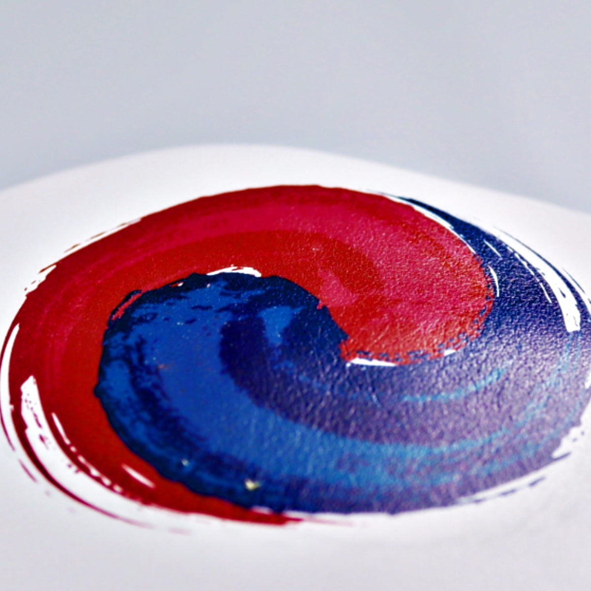 A close-up of a circular painted design on a white surface, featuring a red and blue spiral pattern reminiscent of the South Korean flag.