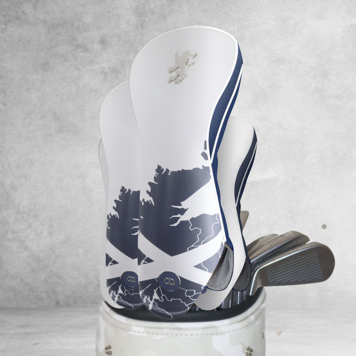 A set of Scotland golf club headcovers cut in white and navy blue nappa leather and set against an abstract background.