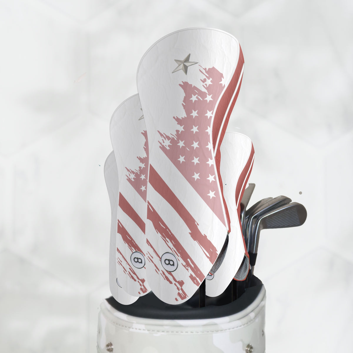 A set of golf club headcover with an American flag design, shown in a white golf bag with golf clubs. The headcovers are white with terracotta brushstroke stripes and white stars, featuring a silver star logo near the top.