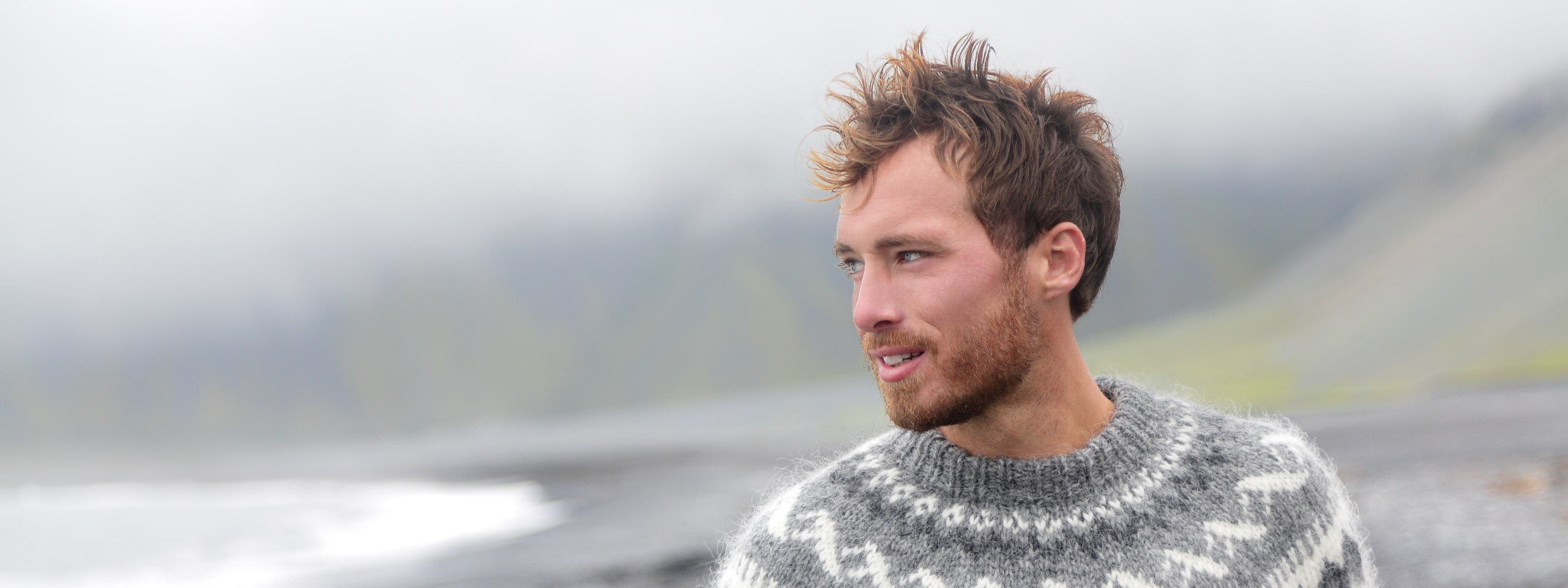 Man wearing a patterned sweater standing outdoors with a blurred natural background