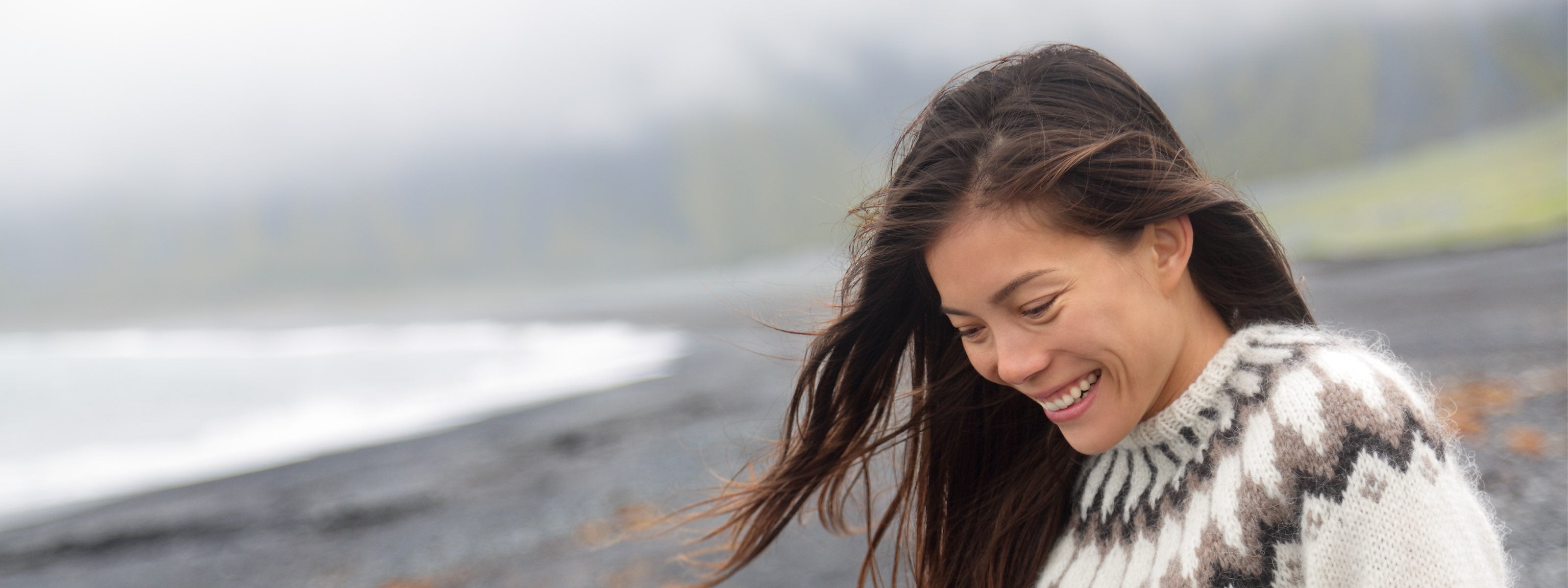 Woman in a patterned sweater standing on a beach with a blurred background